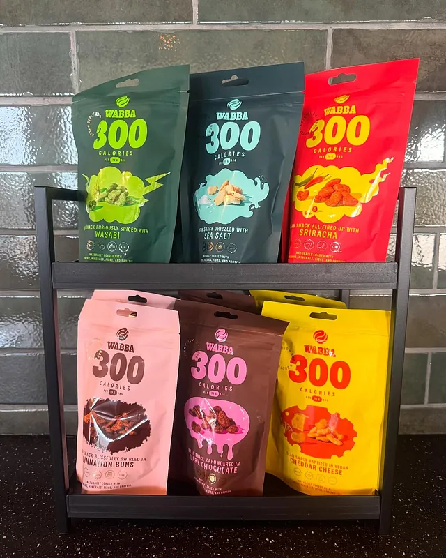 Hylle med seks fargerike poser snacks fra merket WABBA, alle med 300 kalorier per pose.